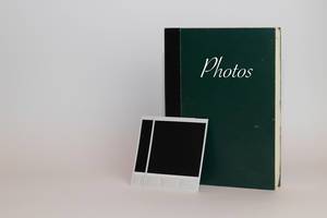 Ein altes Fotoalbum mit Sofortbildern im Vordergrund auf weißem Hintergund