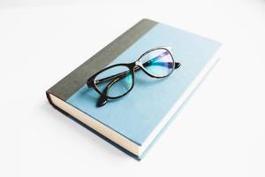 Ein blaues Notizbuch mit einer schwarzen Brille auf weißem Hintergrund