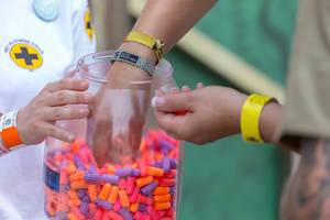 Ein Festivalbesucher nimmt bunte Ohrstöpsel aus einem großen Plastikglas auf Tomorrowland