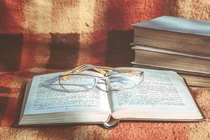 Ein geöffnetes Buch mit Brillen auf bunter Decke