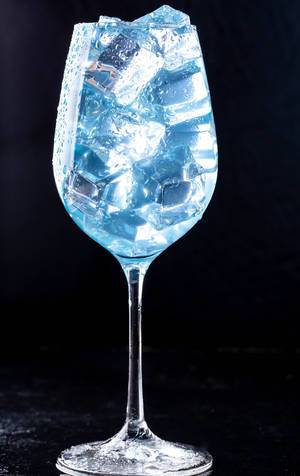 Ein Glas gefüllt mit einem blauen Cocktail und Eiswürfeln vor dunklem Hintergrund
