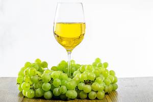 Ein Glas Weißwein, umgeben von grünen Weintrauben, auf einem Holztisch
