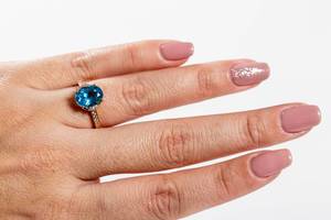 Ein goldener Ring mit einem blauem Topaz an der Hand einer Frau