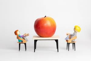 Ein großer roter Apfel auf einem Tisch mit Modelfiguren