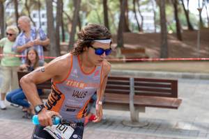 Ein junger Triathlet namens Miquel Valls Alemany mit langen Haaren und Sport-Sonnenbrille läuft beim Peguera Challenge Triatlon 2018