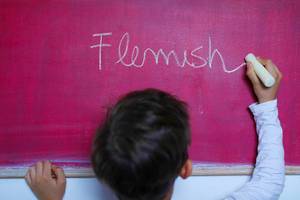 Ein Kind schreibt "Flemish" mit Kreide auf einer pinkfarbenen Tafel