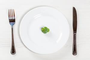 Ein kleines, winziges Stück Brokkoli-Gemüse auf einem weißen Teller, neben Besteck