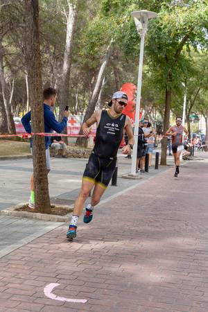 Ein Mann in schwarzem Equipment, Sonnenbrille und Schirmmütze läuft bei einem Triathlon in Paguera