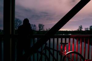 Ein Mann schießt ein Foto von einer Holzbrücke aus, neben einem Fahrrad mit rotem Licht