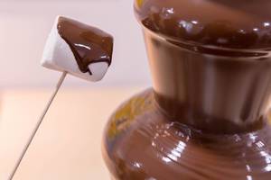 Ein Marshmallow wird in den Schokoladenbrunnen getaucht