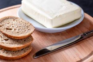 Ein Paket Butter mit ein Paar Scheiben Brot und einem messer auf einem Brettchen