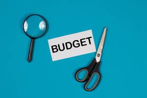 Ein Papier mit der Aufschrift Budget, einer Schere und einer Lupe auf blauem Hintergrund