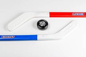Ein Puck liegt zwischen Rotem und Blauem Plastik Hockeyschläger vor weißem Hintergrund Draufsicht
