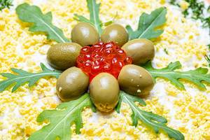 Ein Salat verziert mit Rucola-Blättern, Oliven und rotem Kaviar Nahaufnahme