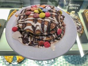 Ein Stapel Pancakes mit Smarties und Schokoladensauce auf einem weißen Tellelr