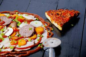 Ein Stück gebackene Fertigpizza neben rohen Zutaten für eine selbstgemachte Pizza