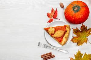 Ein Stück hausgemachter Kürbiskuchen mit frisch gereiften Kürbis-Herbstblättern und einer Gabel auf dem Tisch - Top-view