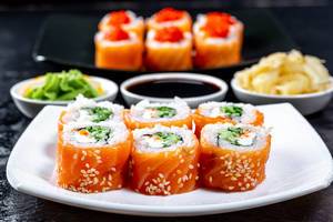 Ein Teller von Sushi Rollen mit Lachs, Sesame, Käse und Gurke serviert mit Wasabi, Sojasoße und Ingwer