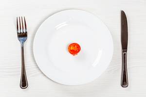 Ein Tomatenstück auf einem weißen Teller, neben Messer und Gabel - Konzeptbild Gewichtsverlust