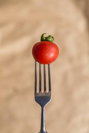 Ein vertikales Foto einer kleinen roten Tomate auf einer Gabel