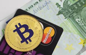 Eine Bitcoin-Münze auf einer schwarzen Kreditkarte und einem Geldschein