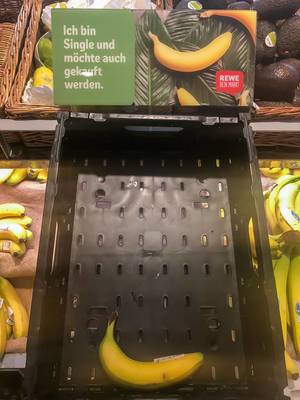 Eine einzelne Banane in einer leeren Kiste zum Verkauf im Supermarkt mit dem Schild "Ich bin Single und möchte auch gekauft werden"