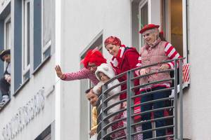 Eine Familie in typischen rot-weißen Kostümen begrüßen den Rosenmontagsumzug in Köln