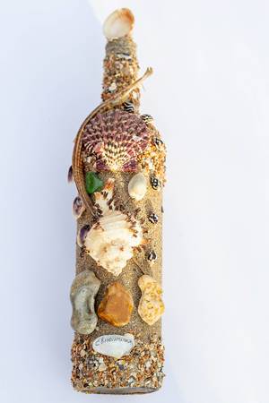 Eine Flasche mit Ozeanschmuck  - Muscheln, Sand und eine Seenadel auf weißem Hintergrund