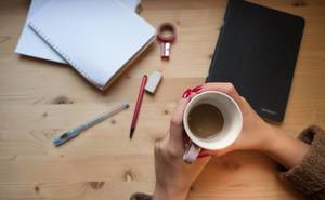 Eine Frau hält eine Tasse Kaffee in beiden Händen über dem Schreibtisch