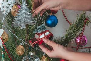 Eine Frau hängt ein Spielzeugauto an den bunt-geschmückten Weihnachtsbaum