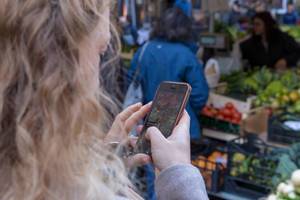 Eine Frau macht ein Foto mit ihrem iPhone von Gemüse auf einem Markt in Rom