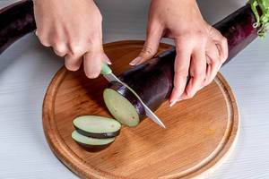 Eine Frau schneidet eine Aubergine mit einem Messer auf einem runden Küchenbrettchen