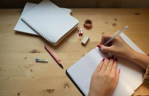 Eine Frau schreibt in einem Notizheft mit Bleistift, Radierer und Anspitzer auf einem Holztisch