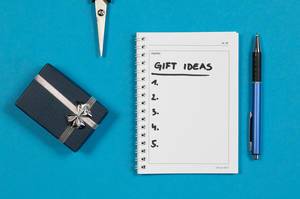 Eine Liste mit Geschenkideen auf einem Notizheft mit einer Schere, Stift und Geschenk auf blauem Hintergrund