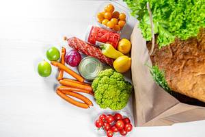 Eine Papiertasche voller Lebensmittel, wie Obst, Gemüse, Würstchen und Konserven