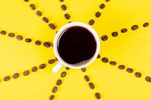 Eine Tasse schwarzer Kaffee auf gelbem Hintergrund mit Kaffeebohnen. Aufnahme von oben