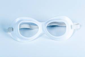 Eine weiße Schutzbrille für chemische Analysen mit Gummiband vor bläulichem Hintergrund