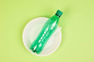 Einweg-Objekte aus Plastik wie Teller, Besteck und PET-Flasche vor hellgrünem Hintergrund