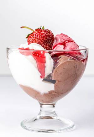 Eiscreme-Schüssel mit Schokoeis, Vanilleeis und Erdbeereis, verziert mit Beerensoße und einer Erdbeere