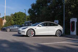 Electric car Tesla Model 3 parks in the shade, in front of Supercharger stations