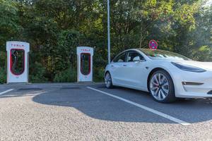 Elektroauto von Tesla parkt im Schatten vor den Supercharger-Ladesäulen
