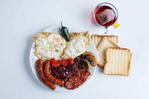 Englisches Frühstück - Ei, Gemüse, Speck und Würste - mit einem Glas Tee Top View