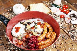 English breakfast in frying pan with ingredients on the table, wooden background