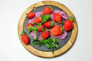 Erdbeeren mit Pfefferminzblättern auf runder Schieferplatte mit Holzrahmen und rosa Netz
