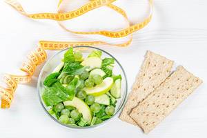 Ernährung-Diätbild mit Knäckebrot und frischen Früchten im grünen Salat, neben einem Körpermaßband