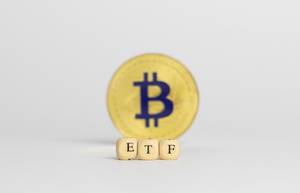 ETF in Buchstaben auf Würfeln mit einem Bitcoin im Hintergrund