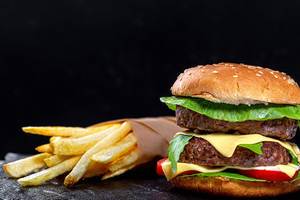 Fast-Food-Konzept: Pommes Frites und doppelter Hamburger mit geschmolzenem Käse, auf schwarzer Oberfläche