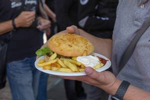 Fast-Food unterwegs essen: Mann trägt einen Teller mit Burger, Pommes, Ketchup und Mayo