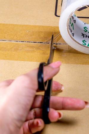 Female hand cuts masking-tape on a cardboard box with black scissors