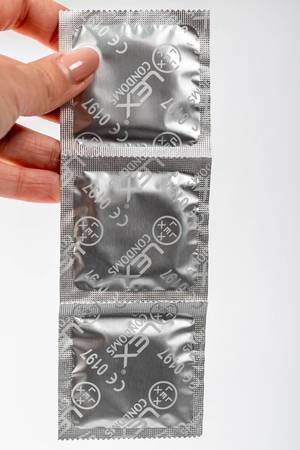 Female hand holding condom package on white background (Flip 2019)